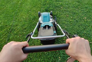 Point of view of a man mowing a lawn with hands on lawn mower and green grass in front