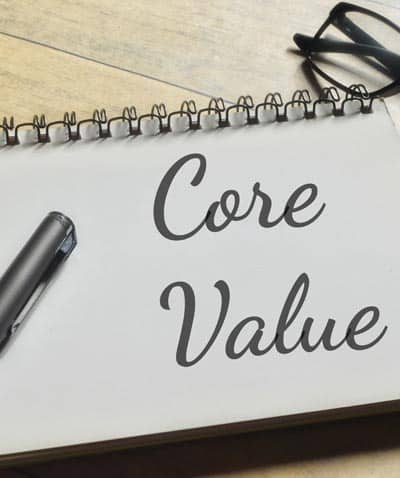 A notepad with the words core value written in cursive with a pen and glasses next to note
