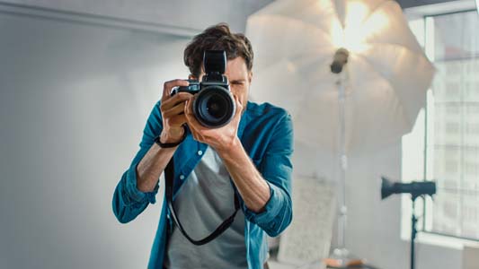 Portrait of photographer holding camera with lens pointing back at the person taking the picture