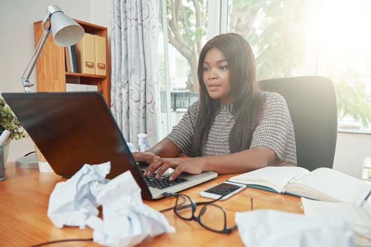 Female copywriter typing on computer to perfect product copy after drafts are now crumbled paper