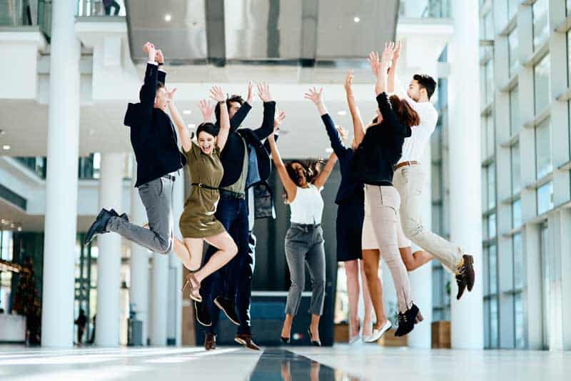 Group of cheerful businesspeople jumping in the air for joy in office after getting sales results