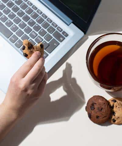 A hand holds bitten cookie next to laptop to indicate real cookies are better than website cookies